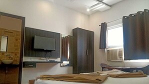 Una habitación de hotel con cama, televisión montada en la pared, armario y ventana con cortinas.