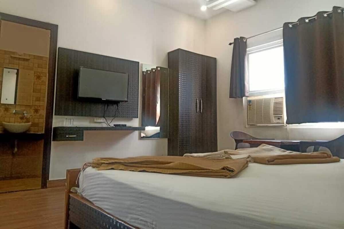 A bedroom with a bed, a TV, a wardrobe, a mirror, and a window with curtains.