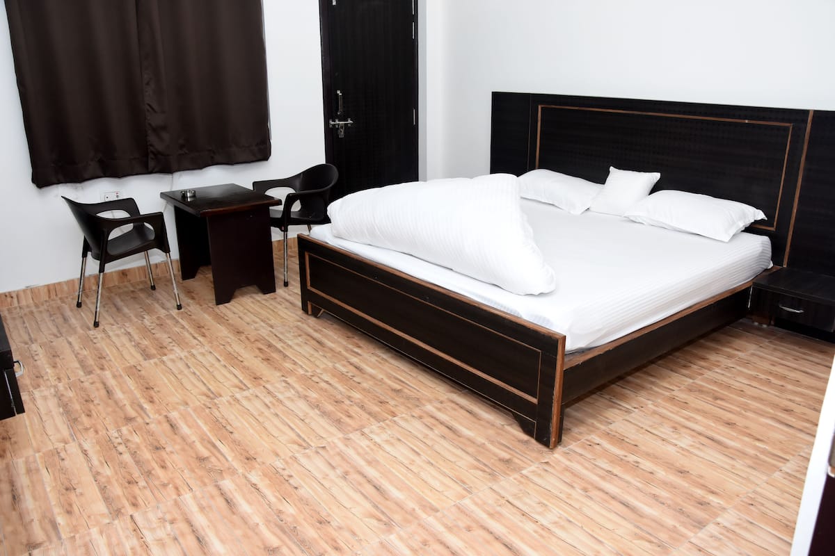 A bedroom with a wooden floor, a bed with white bedding, a desk with a chair, and a wardrobe.