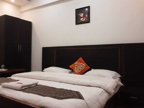 A neatly made bed with white linens, a brown throw blanket, and an orange pillow with a floral design.