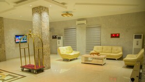 A lobby with a marble floor, a gold cart, a yellow sofa, a white coffee table, and a television on the wall. - Maxbe Continental Hotel (Enugu)