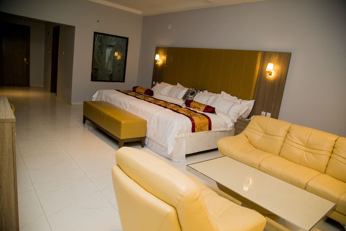 Une chambre d’hôtel avec un lit, deux canapés jaunes, une petite table et un tableau au mur.