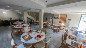 A dining area with multiple tables and chairs, a staircase, and a painting on the wall. - Maxbe Continental Hotel (Enugu)