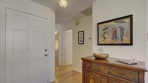 Un couloir avec une commode en bois, un tableau encadré et une porte blanche.