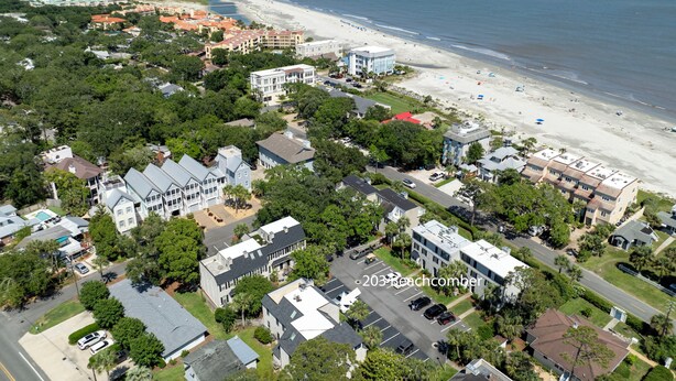 Vue aérienne d’une zone résidentielle côtière, avec des maisons, une plage et un ciel dégagé.