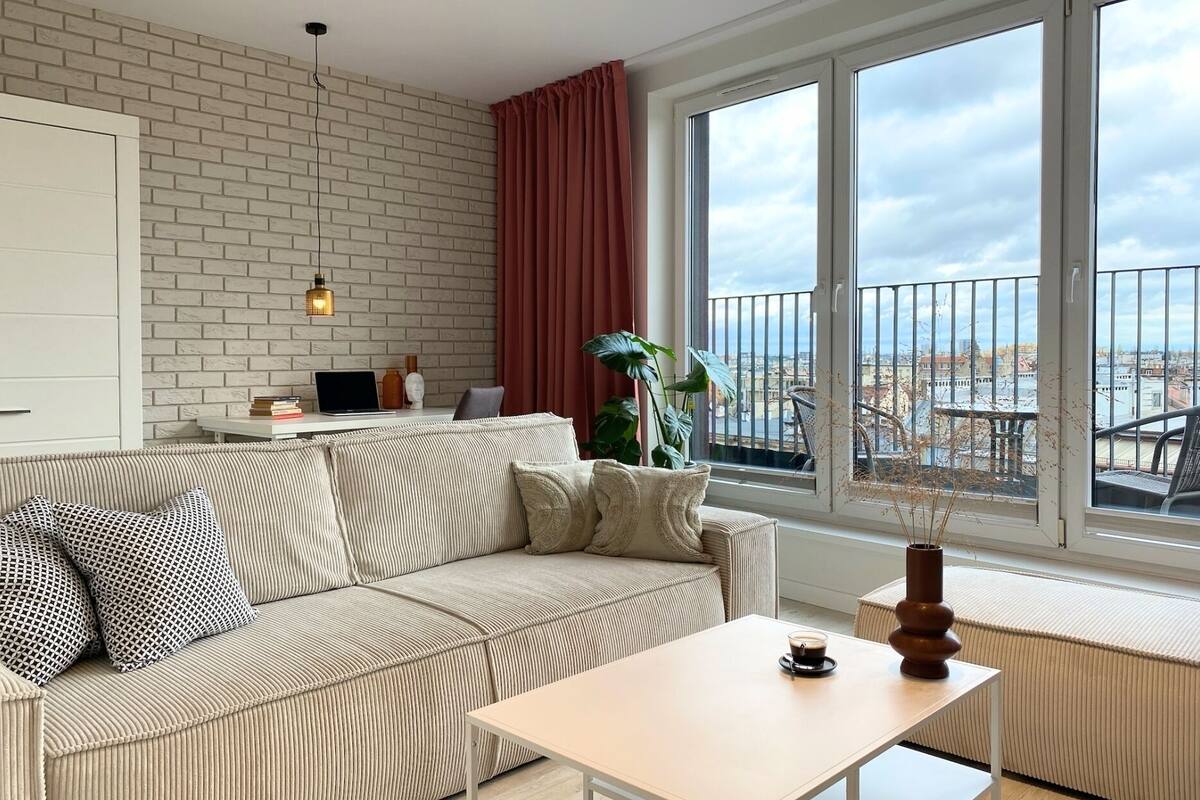 Een moderne woonkamer met een bank, een salontafel en uitzicht op een stadsgezicht door grote ramen.