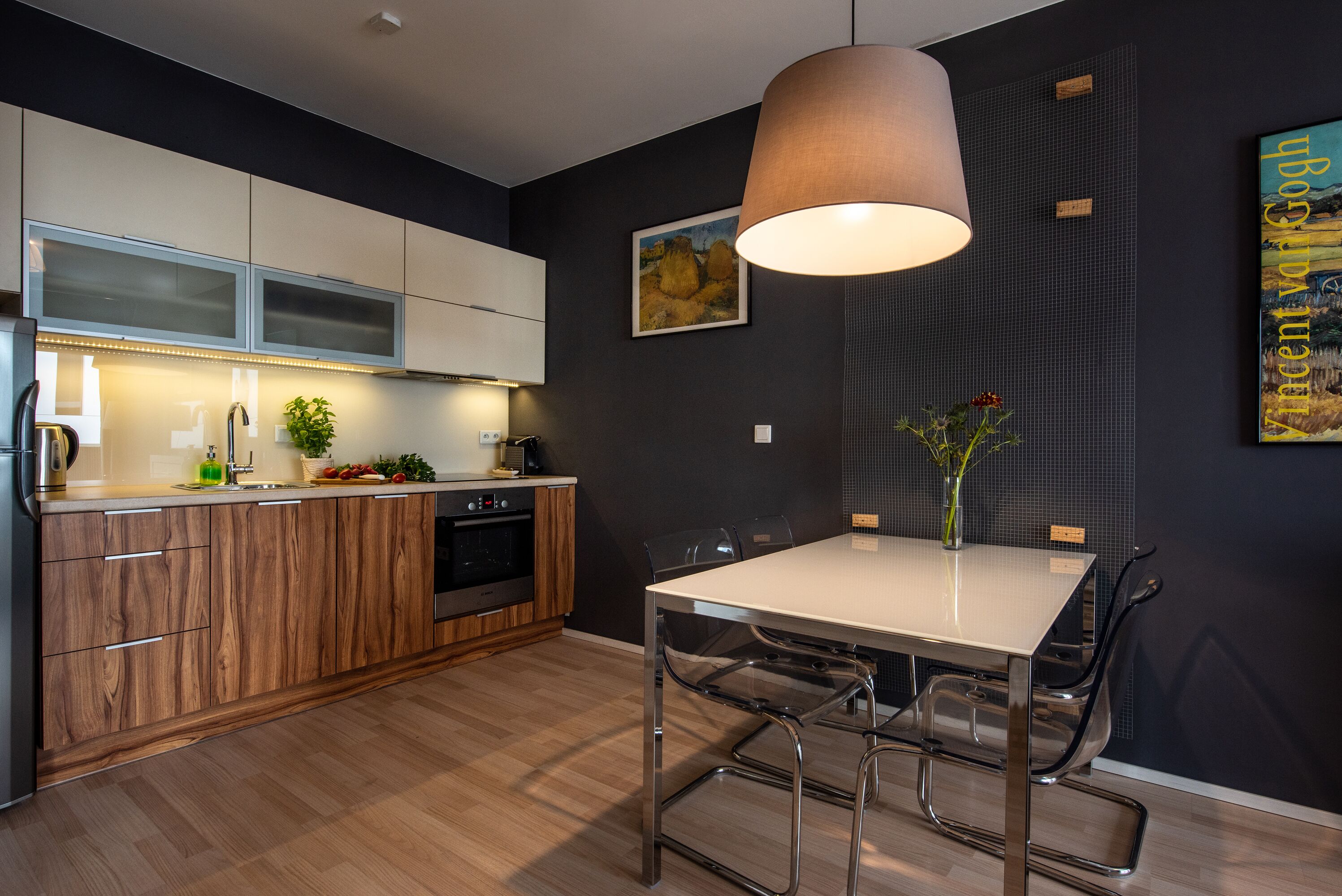 A modern kitchen with wooden cabinets, a dining table with chairs, and a pendant light.