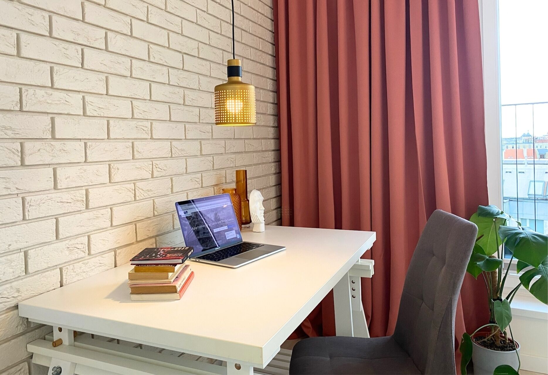 Un espacio de trabajo con una computadora portátil, libros, una planta en maceta y una pared de ladrillo.