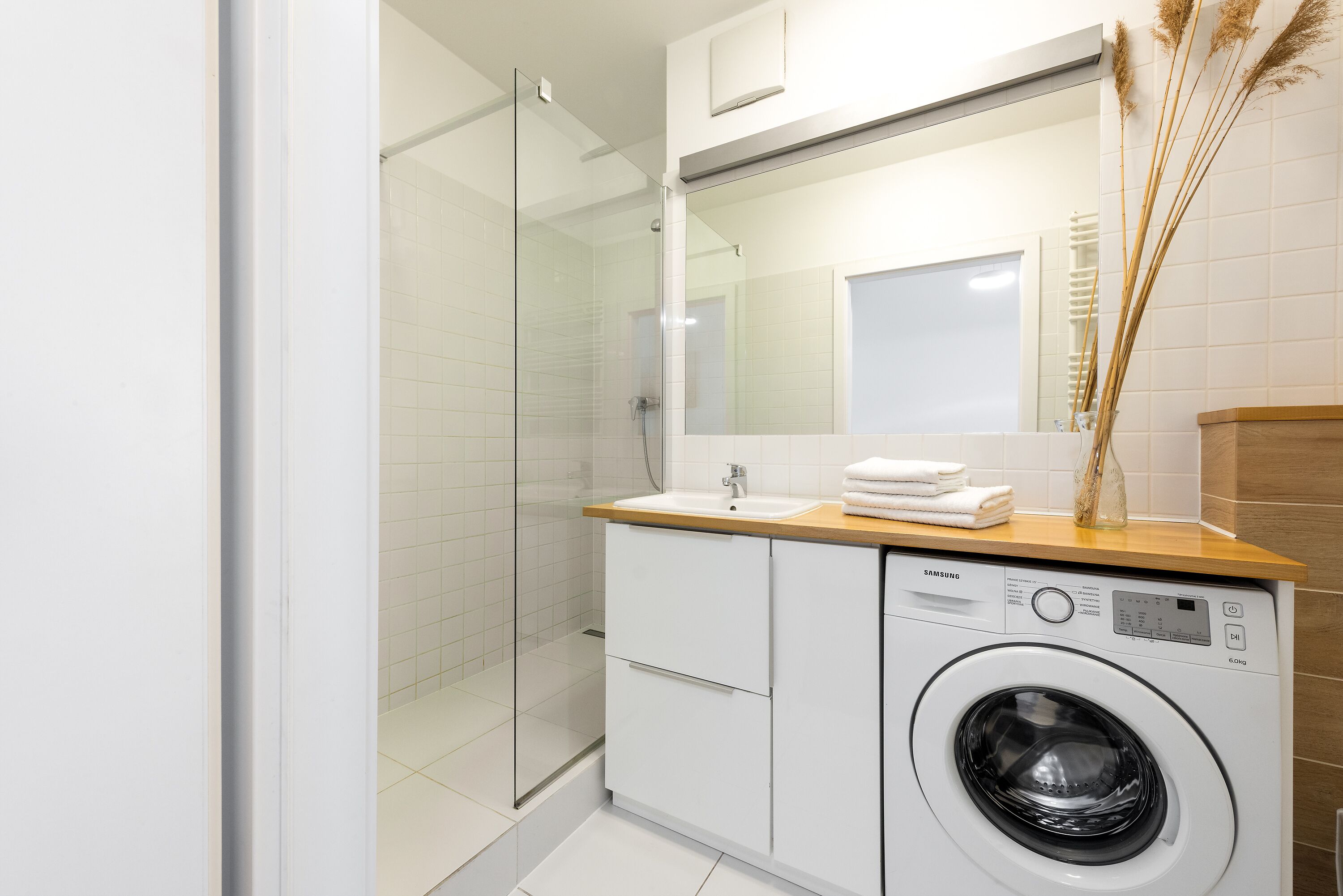 A modern bathroom with a glass shower enclosure, a sink, and a front-loading washing machine.