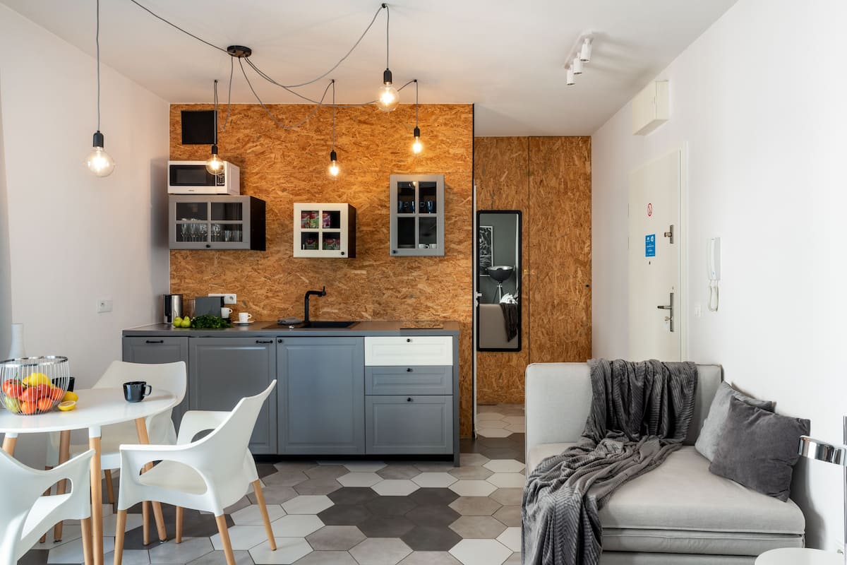 Een kleine keuken met moderne apparaten, een eethoek met witte stoelen en een grijze bank met een plaid.
