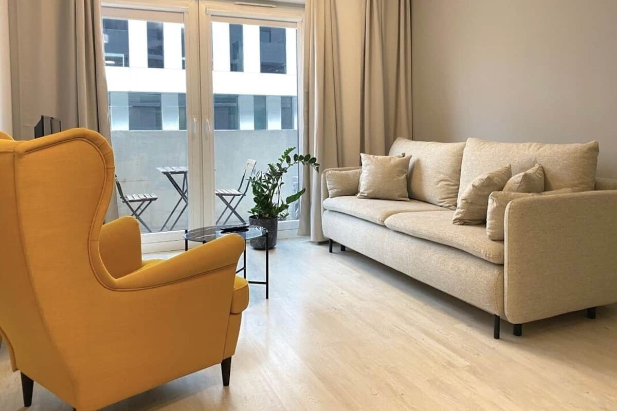 Een moderne woonkamer met een gele fauteuil, een beige bank en een kleine tafel met een plant.