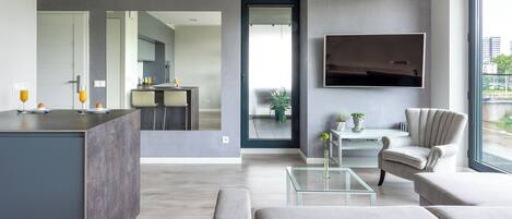 A modern living room with a sofa, a glass coffee table, and a TV mounted on the wall.