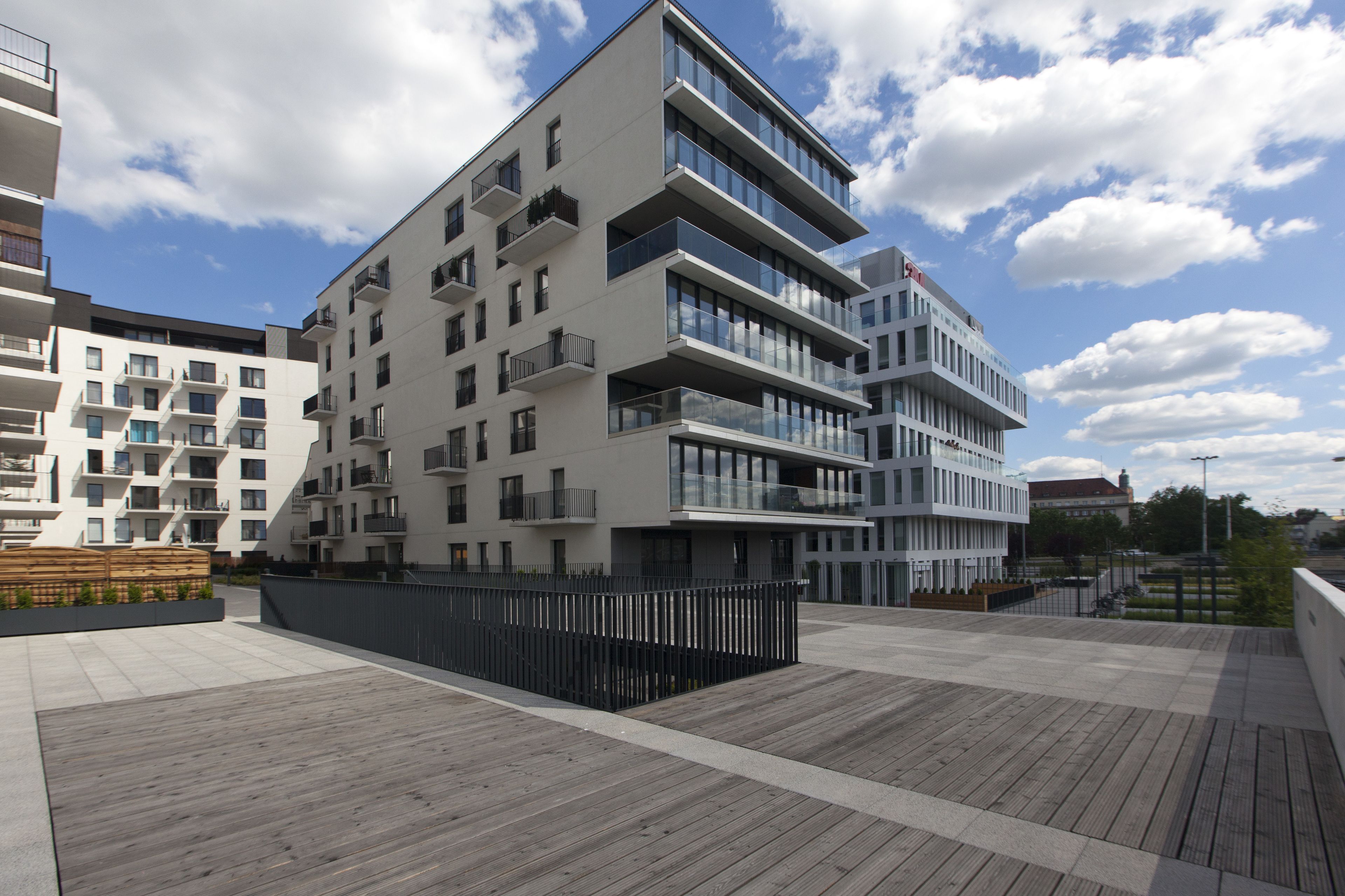 Un immeuble moderne à plusieurs étages, doté de balcons et de grandes fenêtres, situé dans un environnement urbain sous un ciel dégagé.