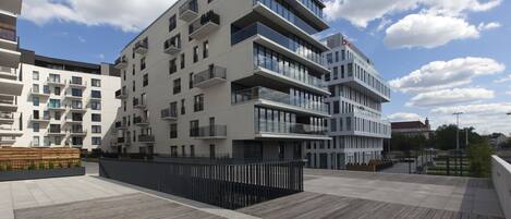 Un immeuble moderne à plusieurs étages, doté de balcons et de grandes fenêtres, situé dans un environnement urbain sous un ciel dégagé.