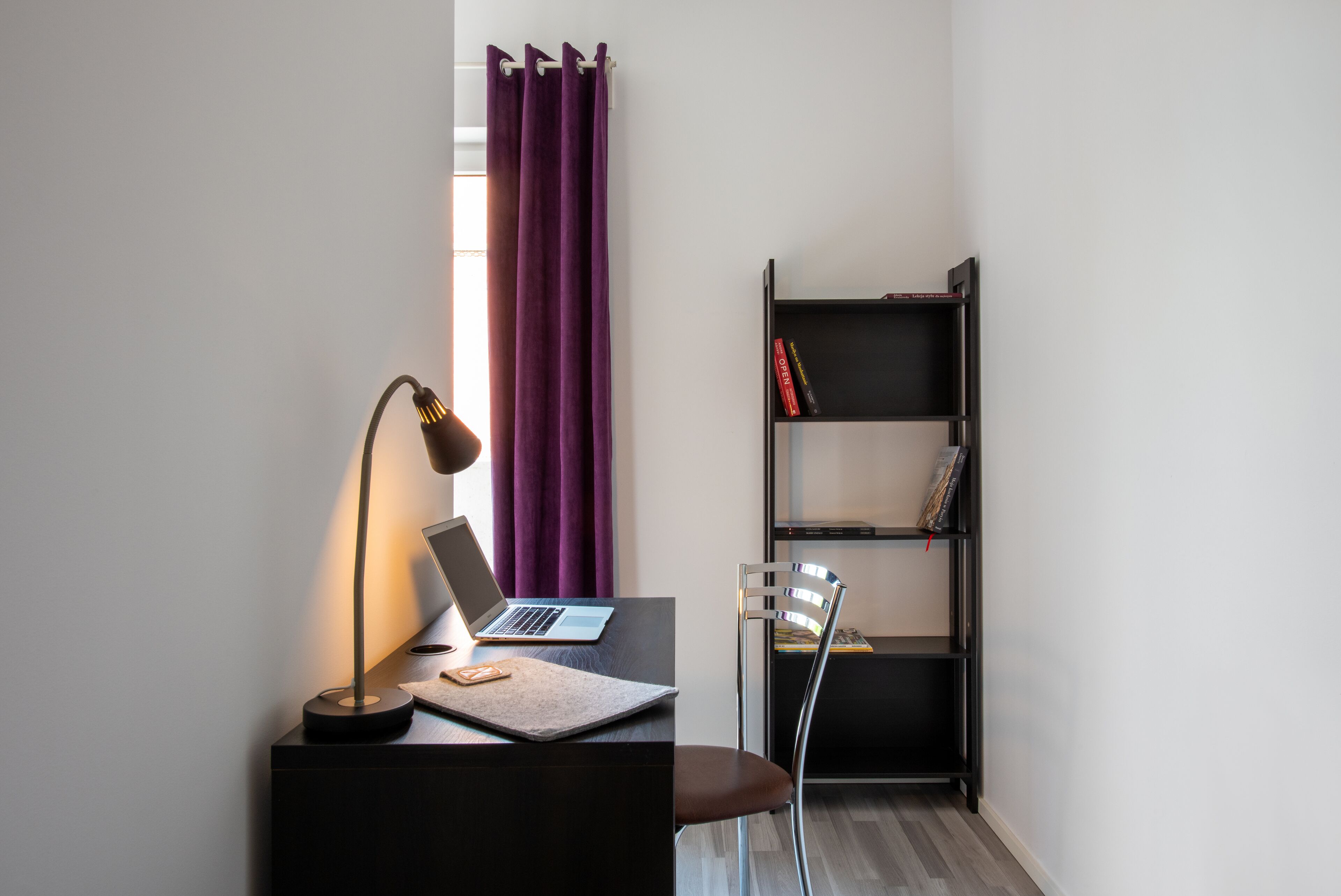 A modern workspace with a laptop, a desk lamp, and a bookshelf.