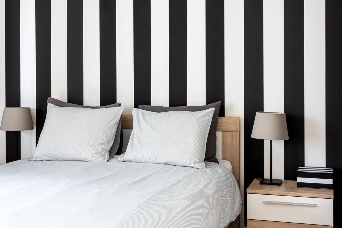 Een bed met witte beddengoed, twee kussens, een nachtkastje met een lamp en een lade.