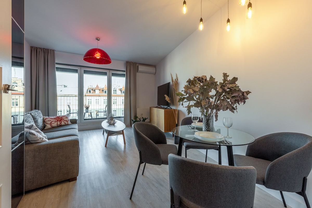 Een moderne woonkamer met een bank, eettafel, stoelen en een rode hanglamp.