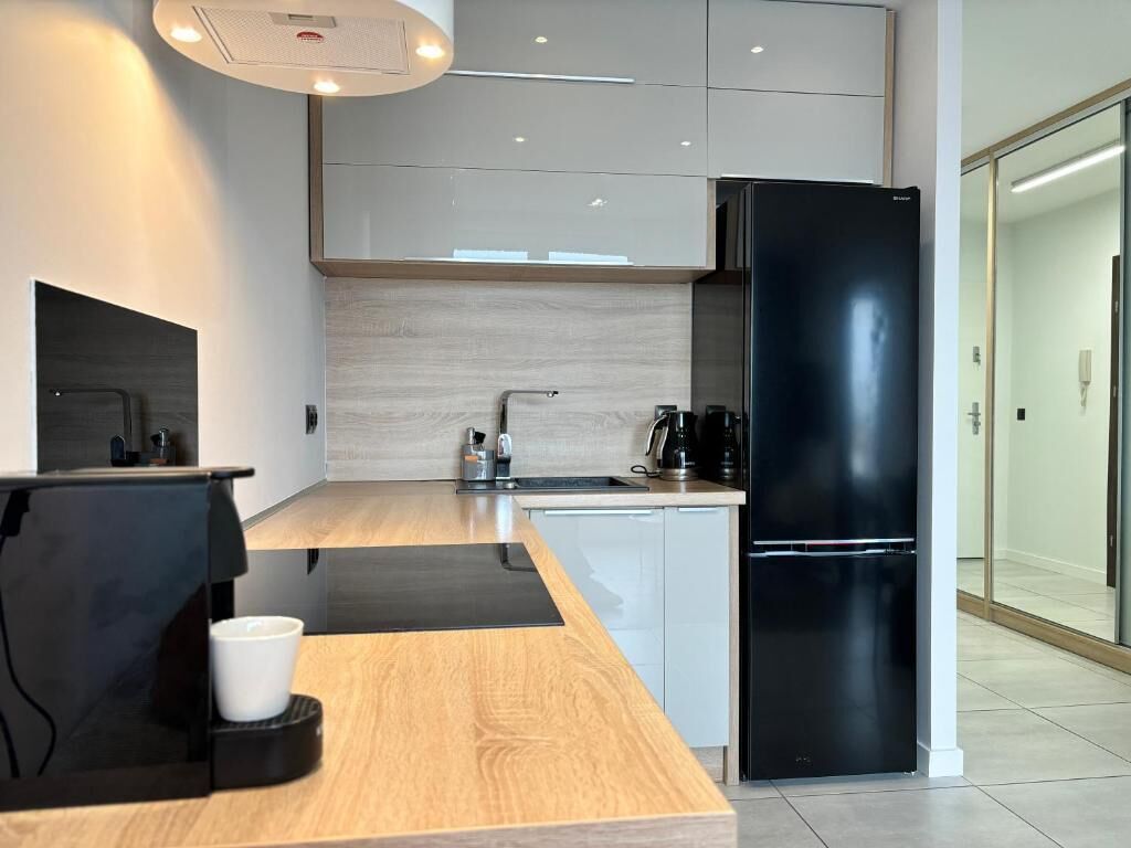 A modern kitchen with a black refrigerator, white cabinets, and a wooden countertop.