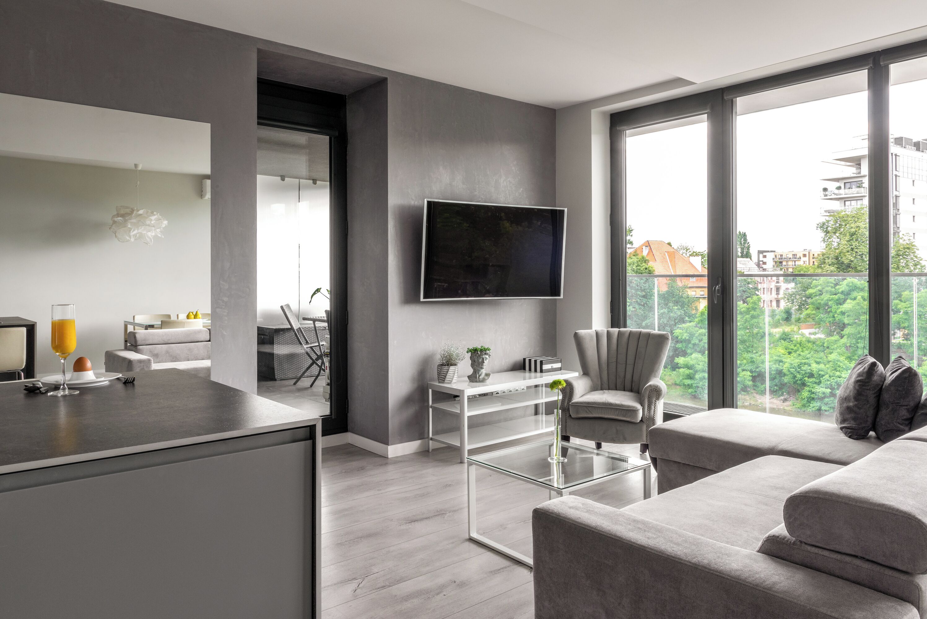 Una sala de estar moderna con un sofá gris, una mesa de centro de vidrio y un televisor de pantalla plana montado en la pared.
