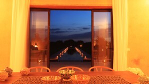 A dining area with a table set for four, a view of a water feature outside, and a sunset in the background. - Pavillon Terra ababila (Marrakech)