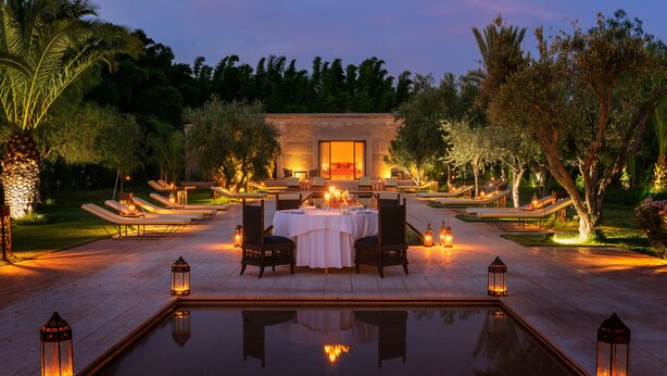 An outdoor dining area with a pool, lounge chairs, and a table set for two. - Pavillon Terra ababila (Marrakech)