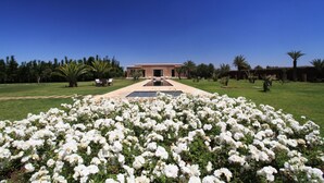 A building with a central courtyard, surrounded by a garden with white flowers and palm trees. - Pavillon Terra ababila (Marrakech)