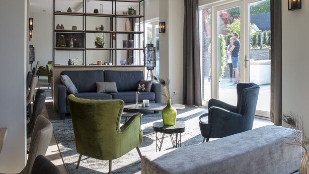 A modern lobby with a sectional sofa, green armchairs, a coffee table, and a bookshelf. - Heuvelrijk Berg en Dal (Groesbeek)