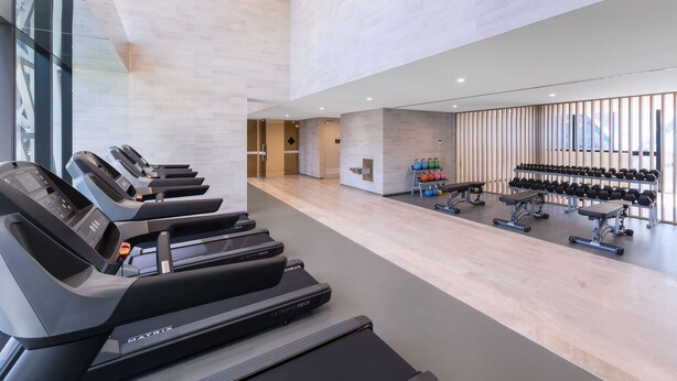 A modern gym with treadmills, weight benches, and dumbbells.