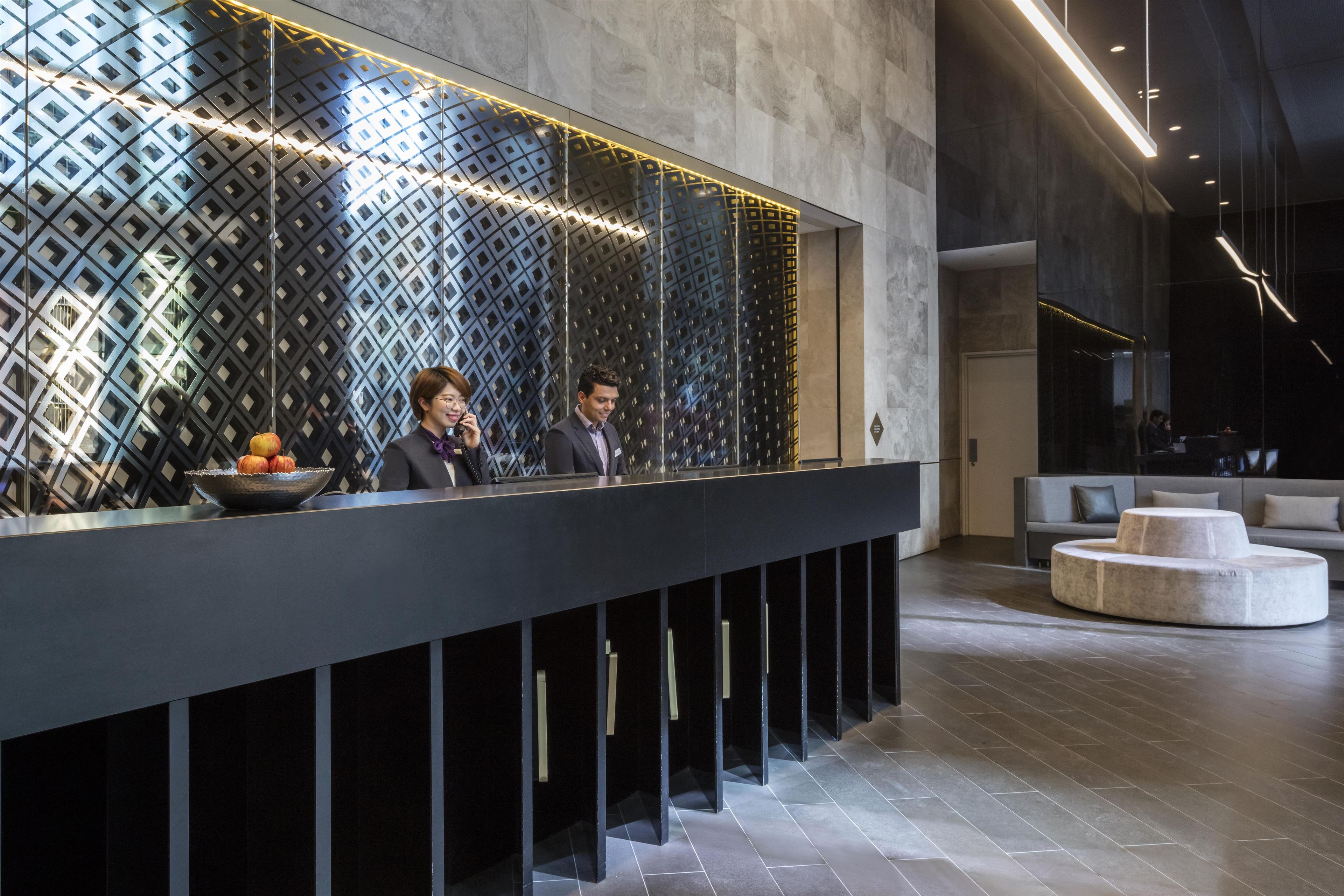A reception area with a modern design, featuring a patterned wall, a reception desk, and a seating area with a sofa and ottoman.