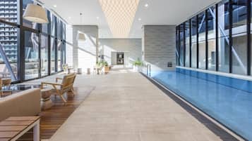 A modern lobby with a pool area, wooden flooring, and seating arrangements.