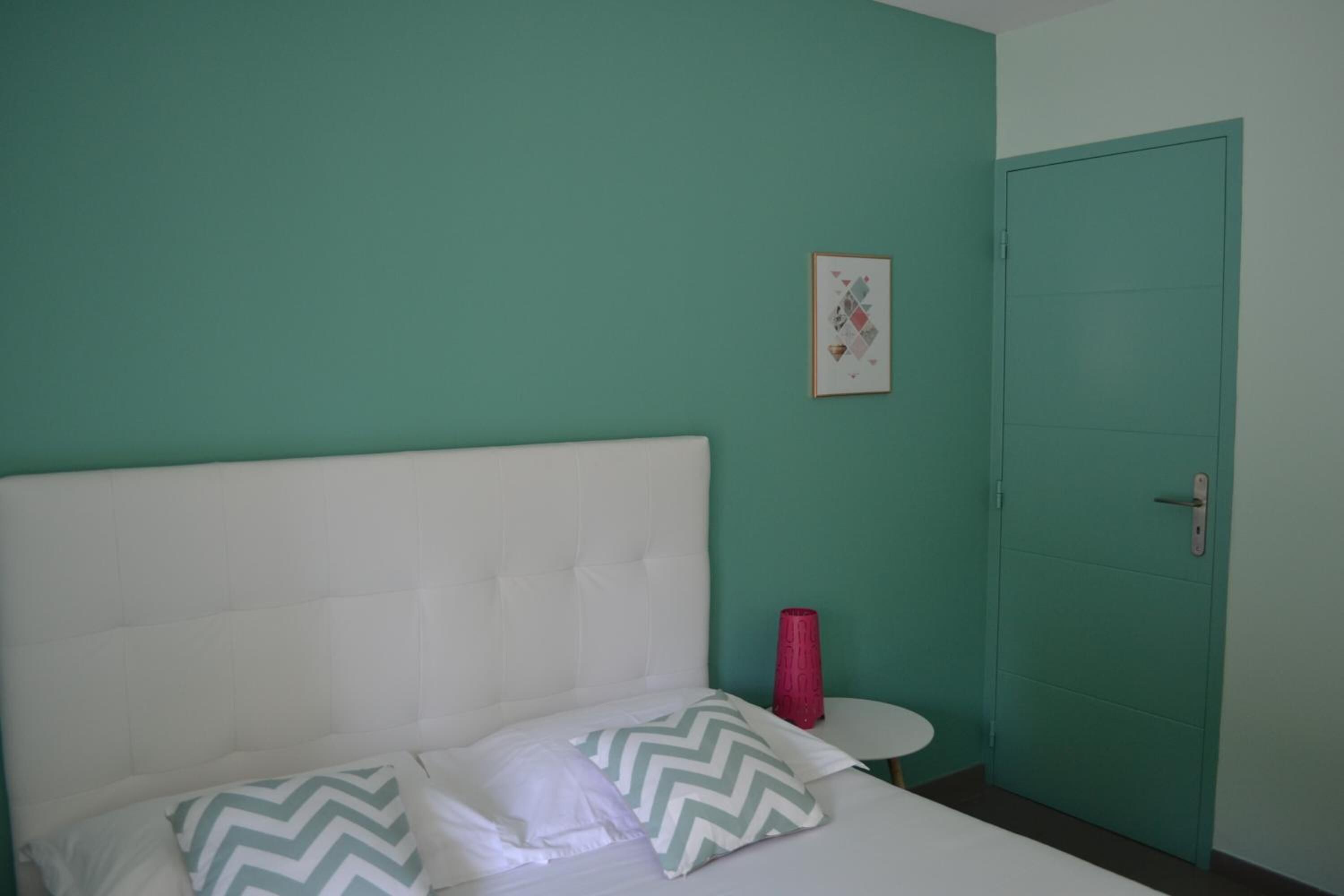 A room with a bed, a small round table, a door, and a framed picture on the wall.