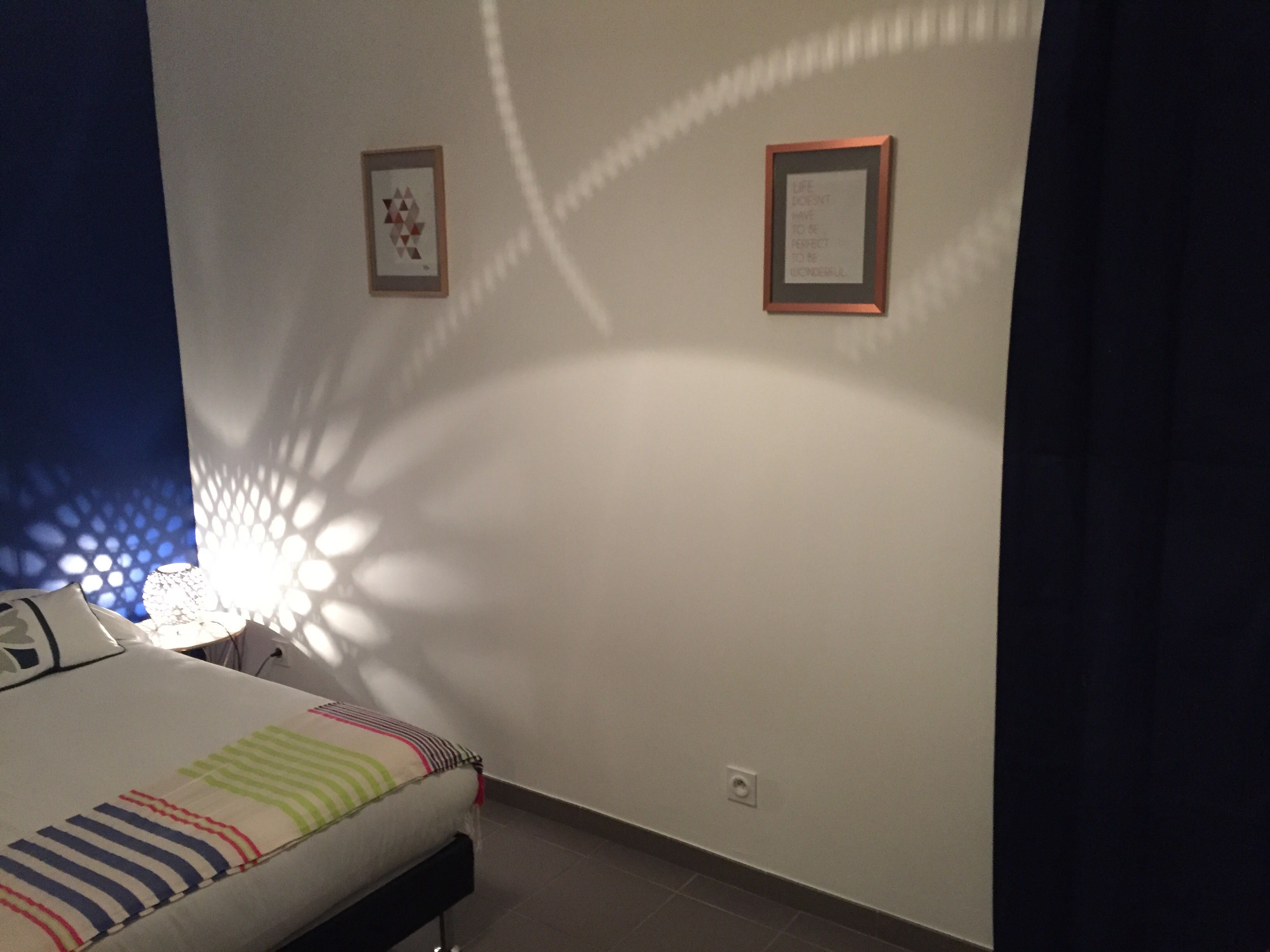 Une chambre à coucher avec un lit, une lampe fixée au mur et deux tableaux encadrés.