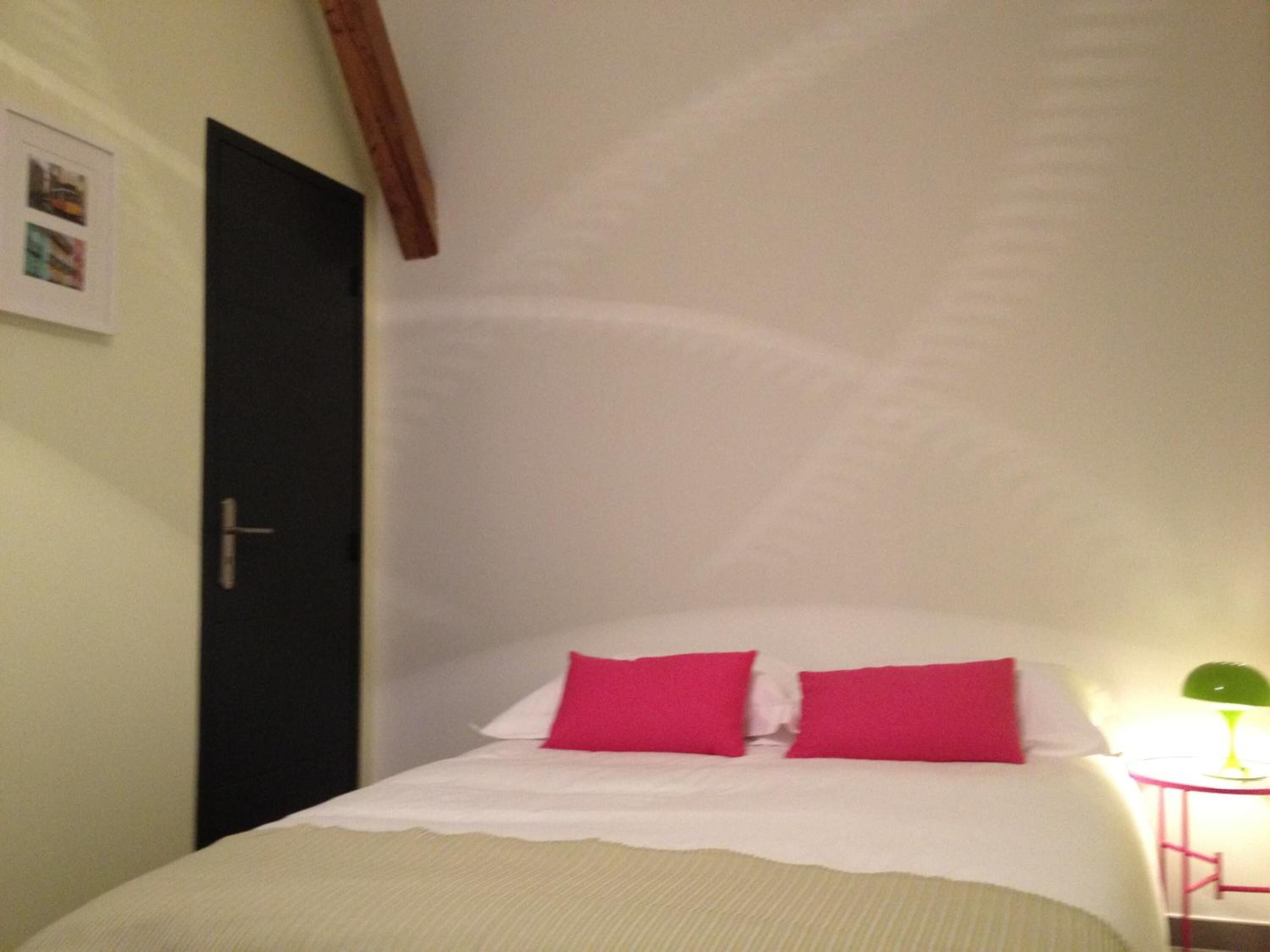 Ein Schlafzimmer mit einem Bett, zwei Kissen, einem Nachttisch mit Lampe und einer Tür.