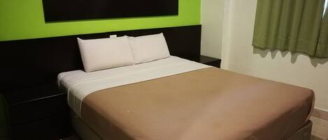 Una cama con cubrecolcha marrón, almohadas blancas y cabecero negro.