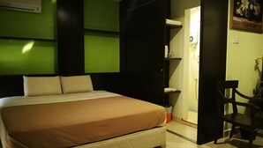 Quarto de hotel com cama, uma cadeira, guarda-roupa e um quadro na parede.