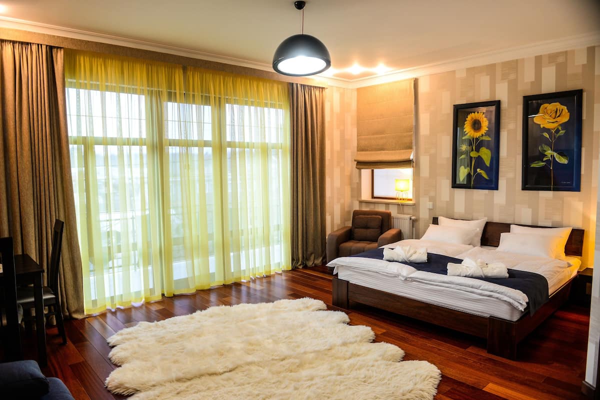 Un dormitorio con una cama grande, una silla, un sofá, una alfombra mullida y dos cuadros en la pared.