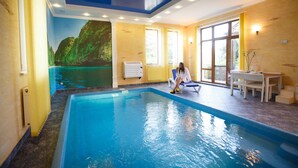 A swimming pool with a mural of a mountainous landscape, a sunlit room with a table and chairs, and a window with curtains. - Premium Village Residence (Hora)