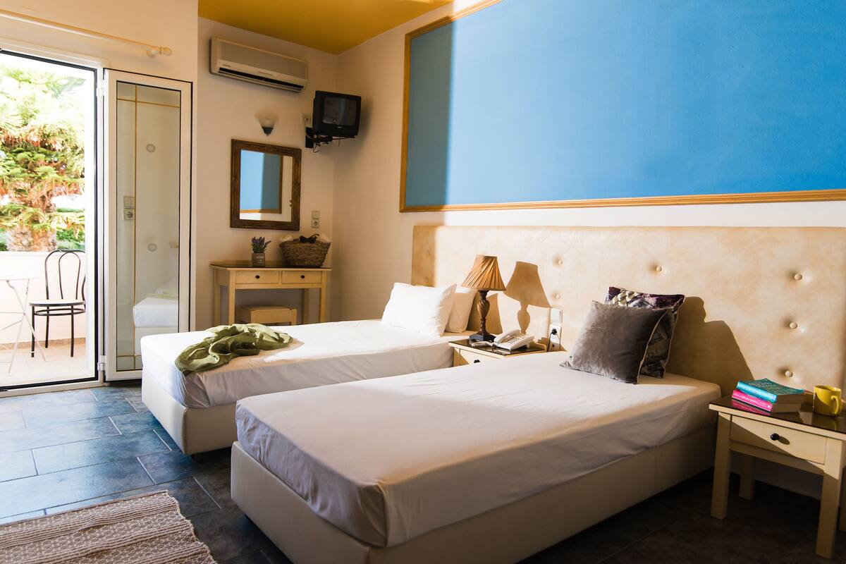 Een hotelkamer met twee bedden, een bureau, een stoel, een televisie en uitzicht op de omgeving.