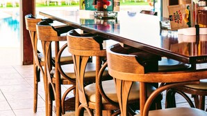 A wooden dining table with chairs, large windows, and a view of a swimming pool and greenery outside. - Yiannis Manos (Hersonissos)