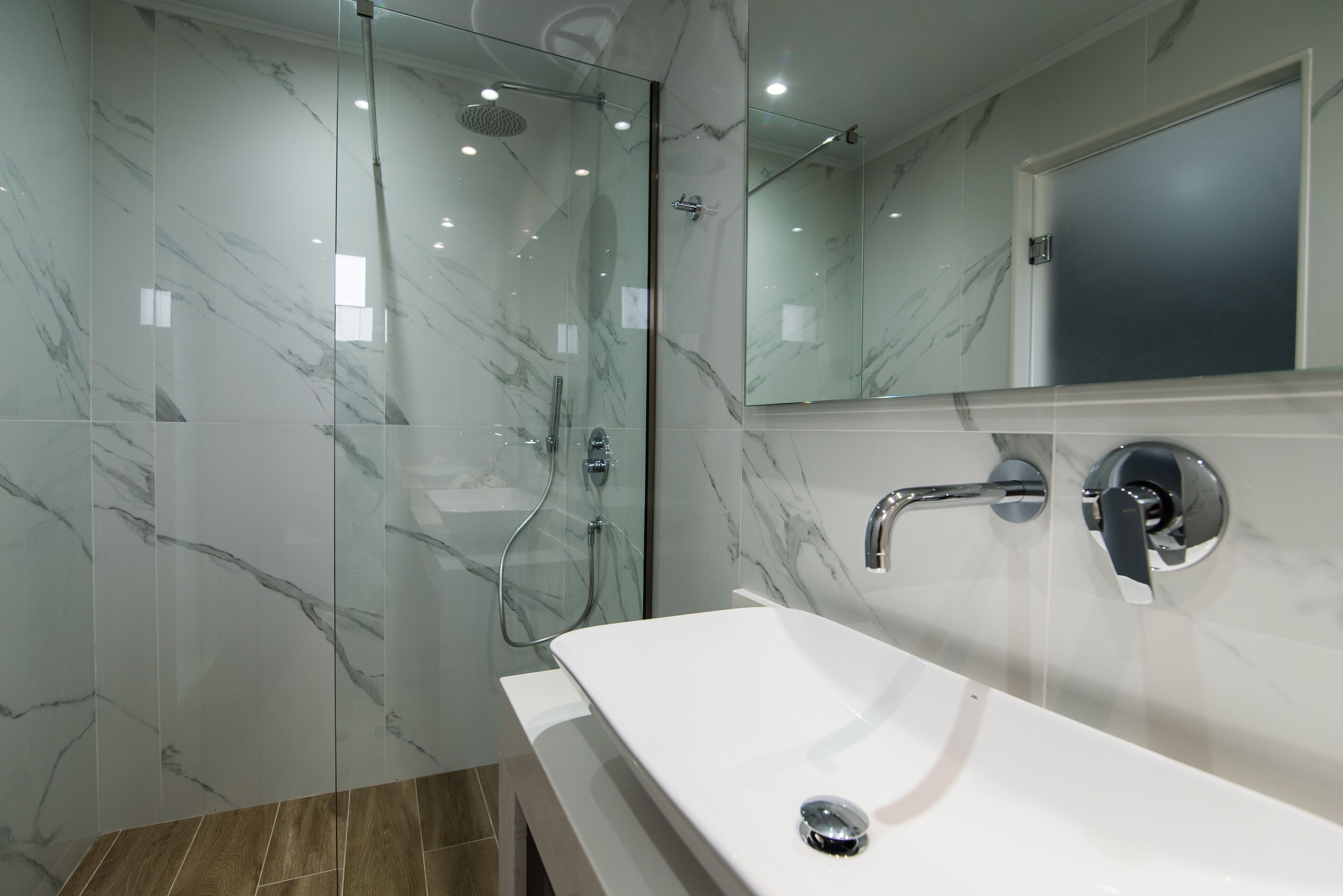 Une salle de bain moderne avec une douche à parois de verre, un lavabo blanc et un grand miroir.