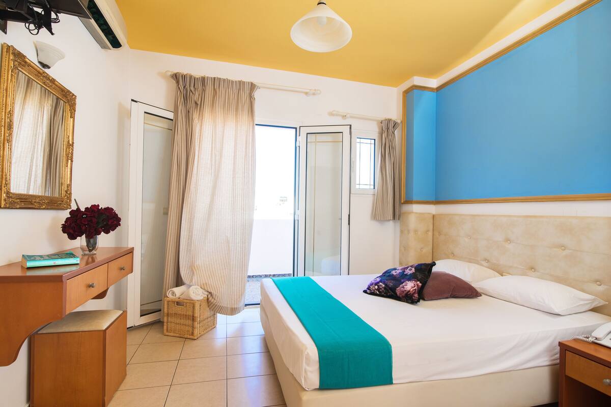 Een hotelkamer met een bed, bureau, stoel, raam met gordijnen en een deur.