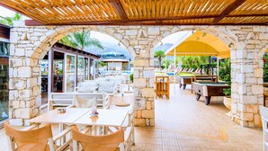 An outdoor patio area with stone arches, wooden tables, and pool tables. - Yiannis Manos (Hersonissos)