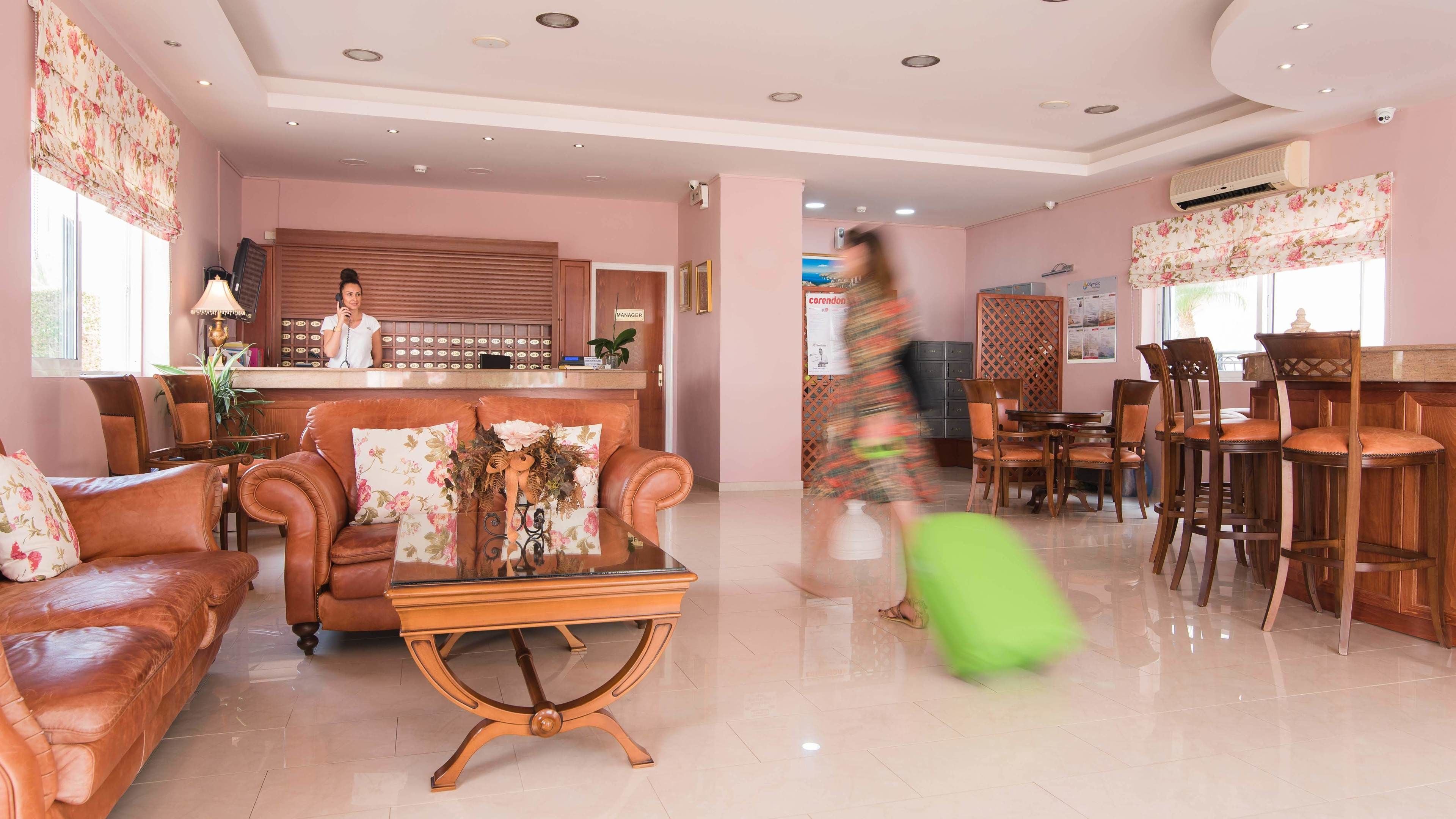 A hotel lobby with leather sofas, a reception desk, and a dining area with wooden chairs and tables.