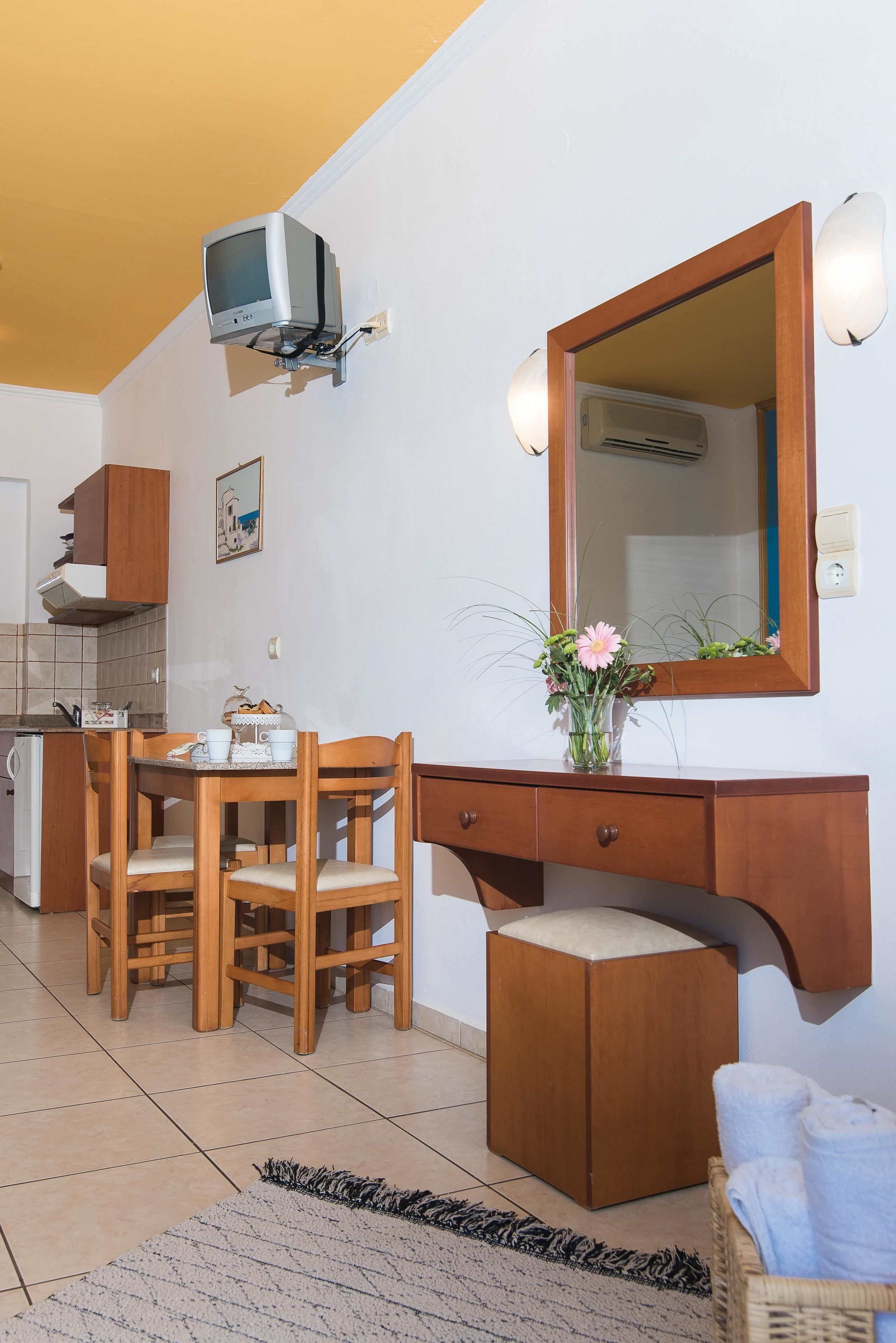A compact living space with a kitchenette, a dining area with wooden furniture, a large mirror, and a small television mounted on the wall.