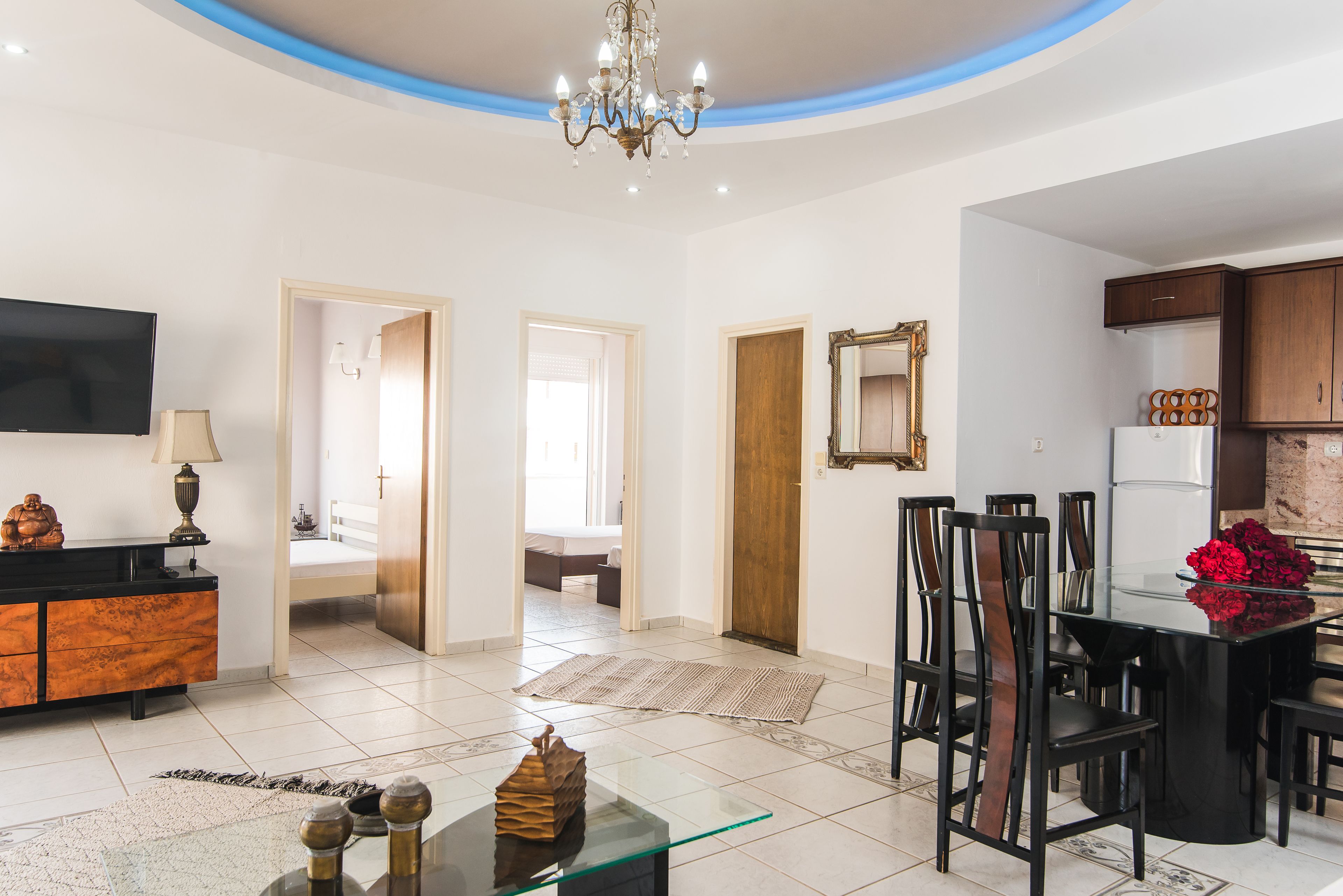 Amplia sala de estar con mesa de comedor de vidrio, sillas negras, televisor y cocina con armarios de madera.