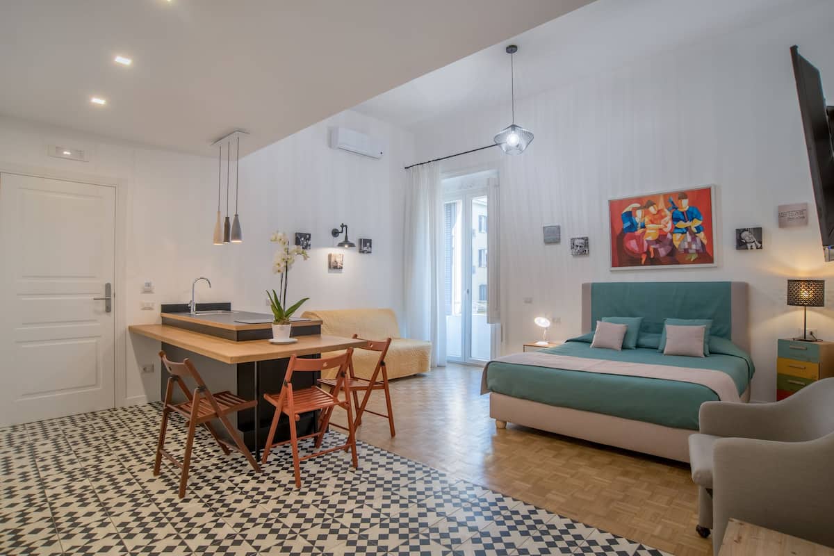 A modern bedroom with a bed, a desk with chairs, and a painting on the wall.