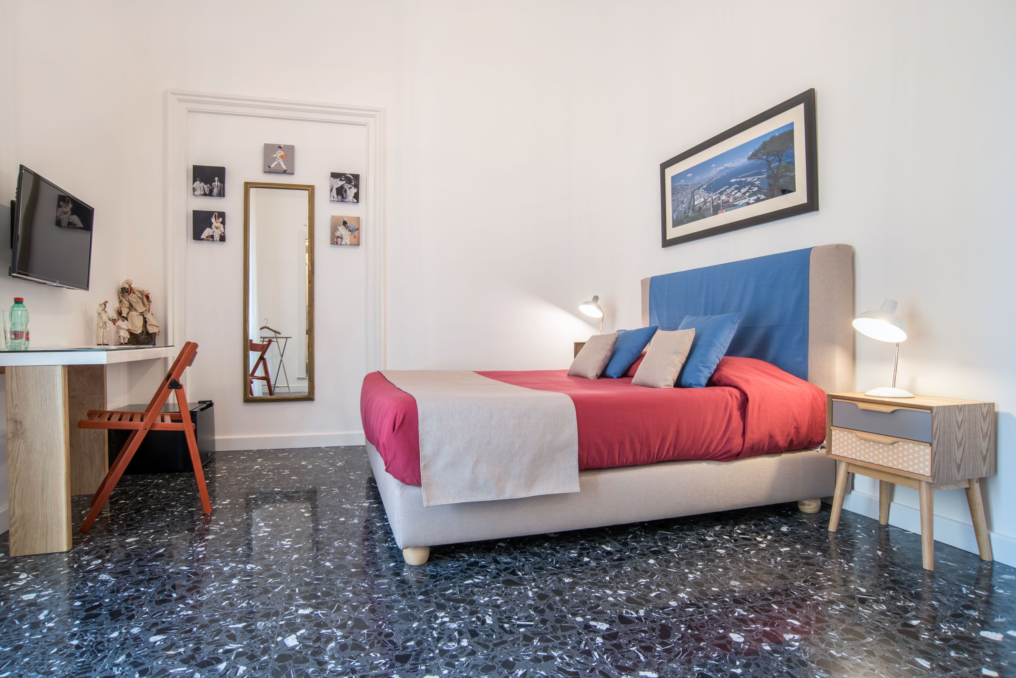 A bedroom with a bed, bedside tables, a desk, a chair, a mirror, and a TV.