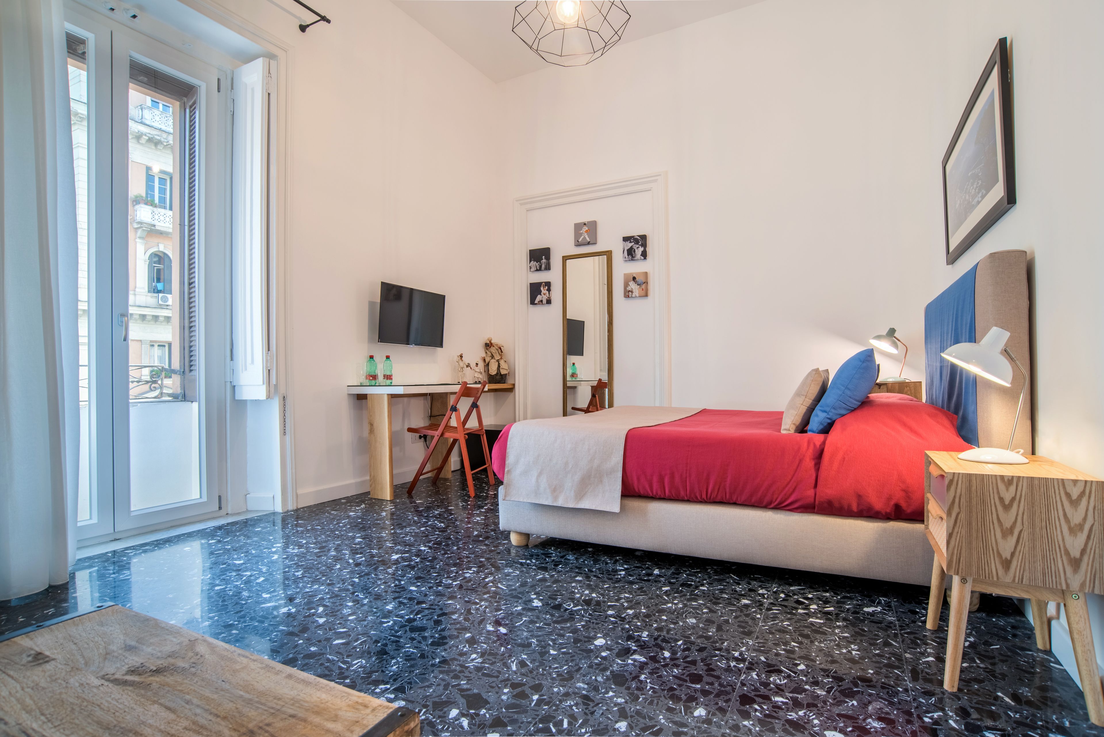 Un dormitorio con una cama, un escritorio, una silla, un televisor y un ventanal amplio.