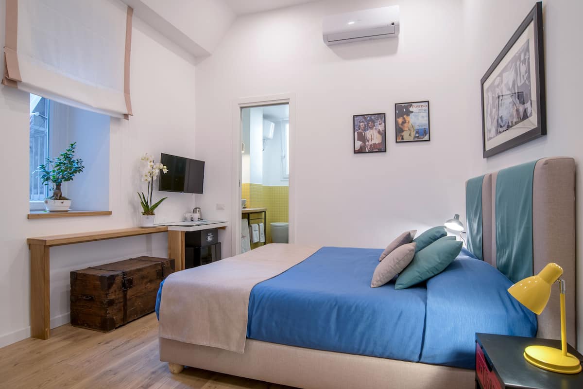 A bedroom with a bed, bedside table, lamp, and a desk with a computer.