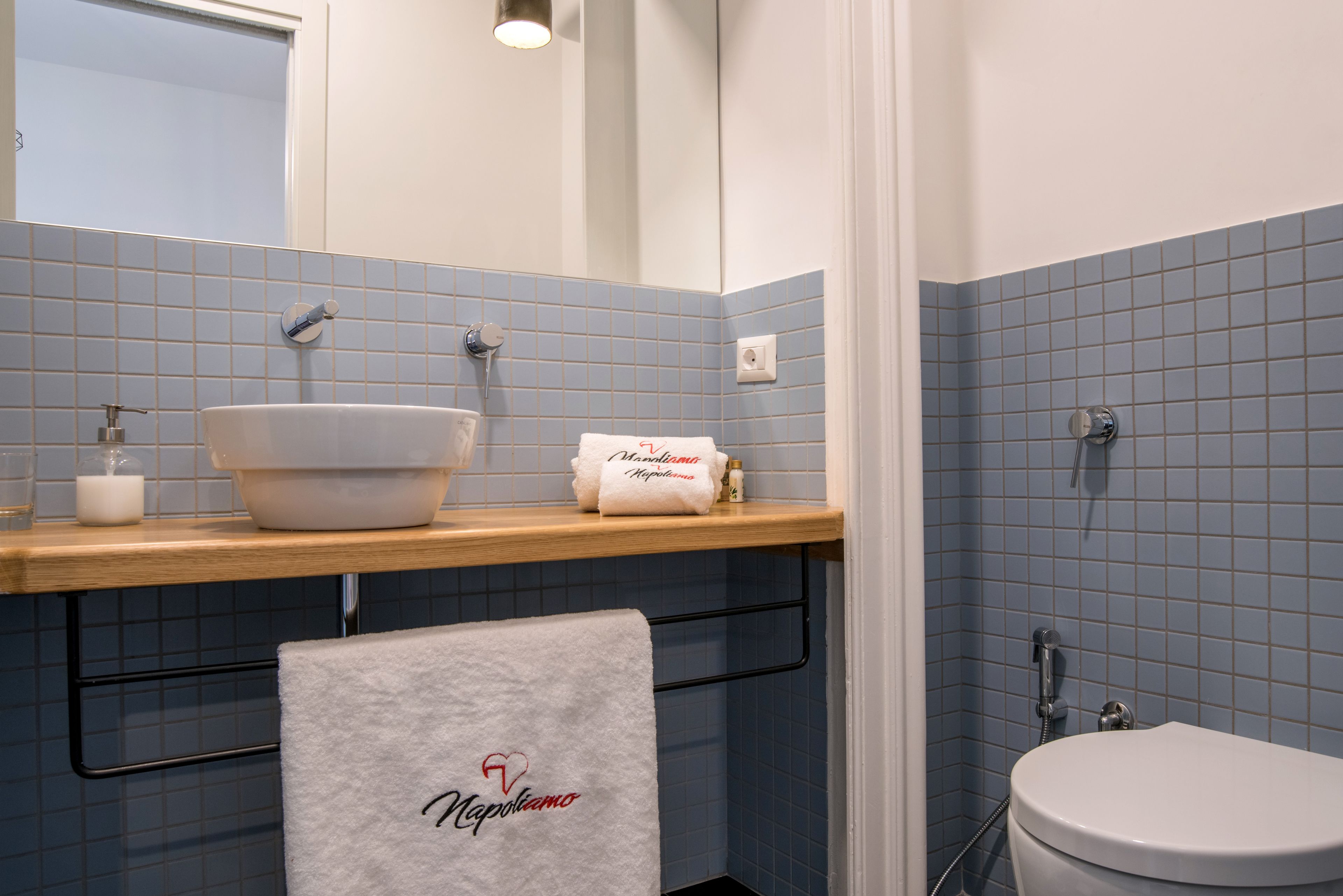 Ein Badezimmer mit Waschbecken, Spiegel und Toilette. Handtücher und Toilettenartikel liegen auf dem Waschbeckenbrett.